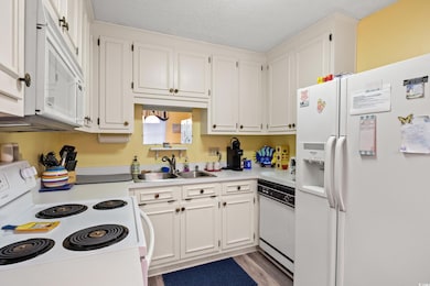 Kitchen with white appliances, a sink, white cabinetry, light countertops, and a textured ceiling