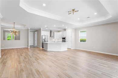 Unfurnished living room featuring a raised ceiling, a chandelier, crown molding, healthy amount of natural light, and light wood-style floors