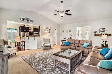 Living area featuring lofted ceiling, a ceiling fan, healthy amount of natural light, and light colored carpet