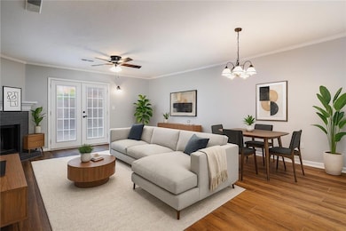 Living room with wood finished floors, ornamental molding, a brick fireplace, ceiling fan, and a chandelier