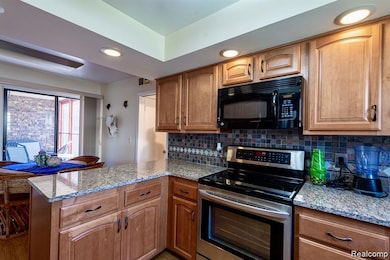Kitchen featuring stainless steel range with electric cooktop, recessed lighting, light stone counters, black microwave, and a peninsula