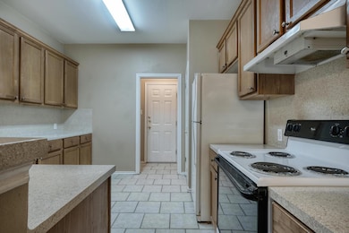 Kitchen featuring electric range oven, under cabinet range hood, light countertops, light tile patterned floors, and brown cabinets