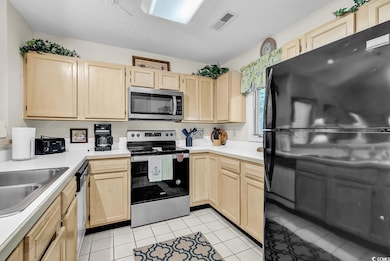 Kitchen featuring appliances with stainless steel finishes, light brown cabinetry, light countertops, and a textured ceiling