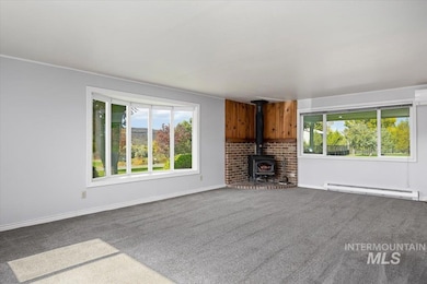 Unfurnished living room with a wood stove, a baseboard radiator, carpet, and a wall mounted air conditioner
