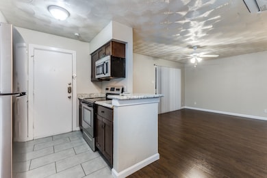 Kitchen with stainless steel appliances, dark brown cabinets, light wood finished floors, ceiling fan, and light stone countertops