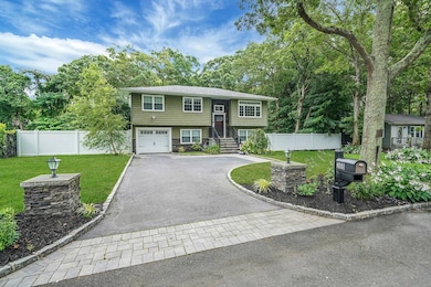 Raised ranch with asphalt driveway, a garage, and view of wooded area