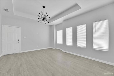 Unfurnished room with a tray ceiling, a chandelier, light wood finished floors, and baseboards