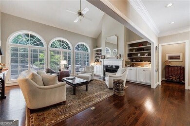 Living area with built in features, ceiling fan, dark wood-style floors, a fireplace, and ornamental molding