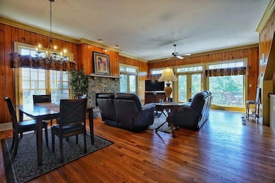 Dining area with wooden walls, wood finished floors, ornamental molding, a ceiling fan, and a stone fireplace