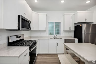 Kitchen with stainless steel appliances, light wood-style flooring, white cabinetry, recessed lighting, and light stone countertops