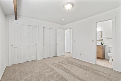 Primary bedroom with two closets, NEW carpet & pad, ensuite bathroom, and beam ceiling