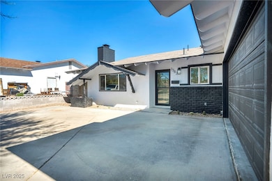 Rear view of property with brick siding, a chimney, a patio, a shingled roof, and stucco siding