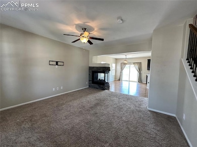 Unfurnished living room featuring carpet floors, ceiling fan, a multi sided fireplace, and stairway