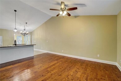 Unfurnished living room featuring wood finished floors, a ceiling fan, vaulted ceiling, and a chandelier