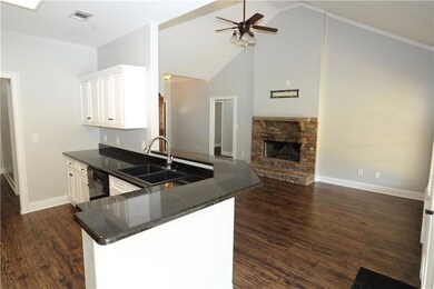 Kitchen featuring dark wood-type flooring, white cabinets, dark stone counters, high vaulted ceiling, and a stone fireplace