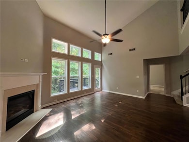Unfurnished living room with ceiling fan, stairway, wood finished floors, a glass covered fireplace, and a towering ceiling