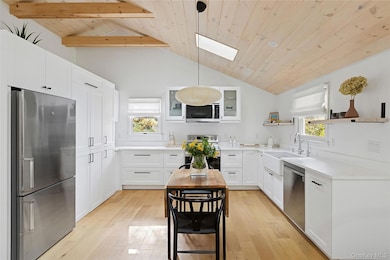 Kitchen with appliances with stainless steel finishes, wood ceiling, white cabinets, hanging light fixtures, and a skylight