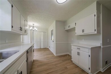 Kitchen featuring stainless steel dishwasher, white cabinets, a chandelier, light wood finished floors, and a textured ceiling