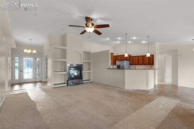 Unfurnished living room with light carpet, a chandelier, a multi sided fireplace, high vaulted ceiling, and ceiling fan