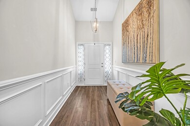 Entryway with dark wood-type flooring, a decorative wall, a towering ceiling, and wainscoting