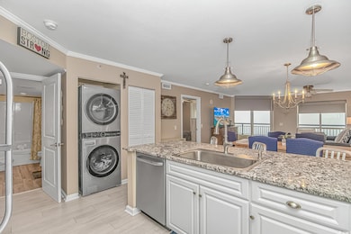 Kitchen with ornamental molding, white cabinetry, light stone counters, stainless steel dishwasher, and a chandelier