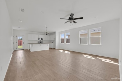 Unfurnished living room with a ceiling fan, light wood-style flooring, and a chandelier