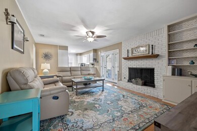 Living room with a brick fireplace, wood finished floors, a ceiling fan, and french doors