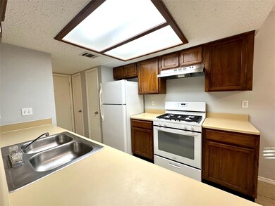 Kitchen with white appliances, light countertops, a textured ceiling, and under cabinet range hood
