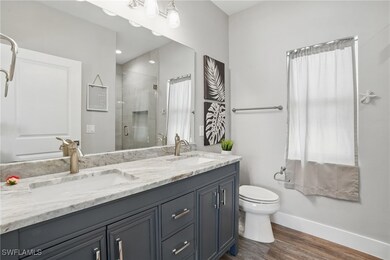 Bathroom with baseboards, double vanity, wood finished floors, a stall shower, and toilet