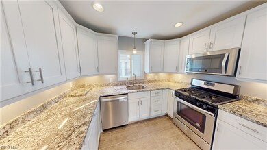 Kitchen with sink, light tile flooring, pendant lighting, stainless steel appliances, and white cabinets