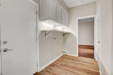 Just off the kitchen, this utility area provides dedicated washer and dryer connections. The upper cabinetry offers convenient storage for laundry essentials, and the door to the left leads directly to the attached garage — making unloading groceries a breeze.