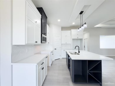 Kitchen featuring white cabinetry, sink, an island with sink, and decorative light fixtures