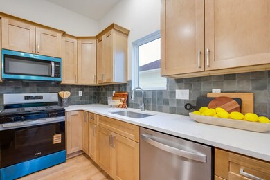 Kitchen featuring stainless steel appliances, decorative backsplash, light wood-style flooring, light stone countertops, and light brown cabinetry