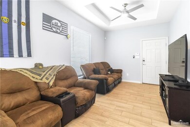 Living area featuring a tray ceiling, ceiling fan, light wood-style flooring, baseboards, and a skylight