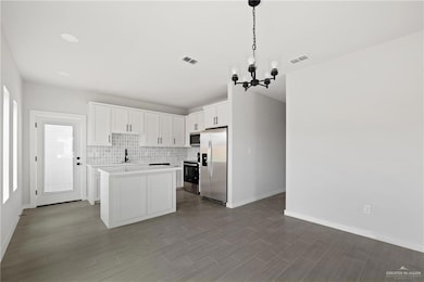 Kitchen featuring stainless steel appliances, a chandelier, light countertops, white cabinets, and tasteful backsplash