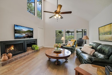 Living area with a lit fireplace, wood finished floors, high vaulted ceiling, and a ceiling fan