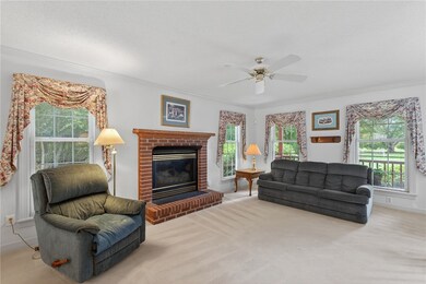 Living area featuring a brick fireplace, ornamental molding, light colored carpet, and a ceiling fan