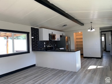 Kitchen featuring a peninsula, white cabinets, light wood-type finish flooring, hanging light fixtures, and appliances with stainless steel finishes.