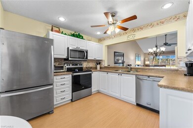 Kitchen with a sink, ceiling fan with notable chandelier, light wood-style floors, backsplash, and appliances with stainless steel finishes