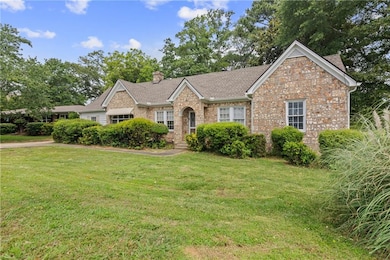 Ranch-style house with a front yard, a chimney, a shingled roof, and brick siding