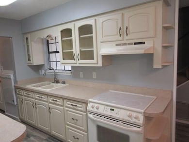 Kitchen with white electric stove, under cabinet range hood, a sink, open shelves, and light countertops