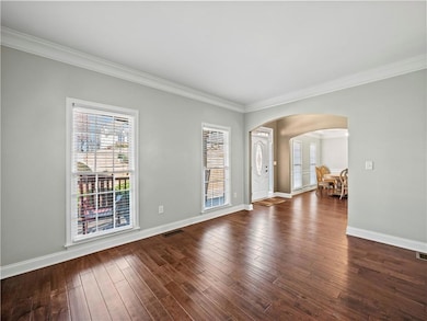 Spare room featuring crown molding, arched walkways, plenty of natural light, and dark wood-type flooring