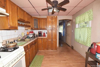 Kitchen with white gas stove, a paneled ceiling, brown cabinetry, decorative backsplash, and arched walkways