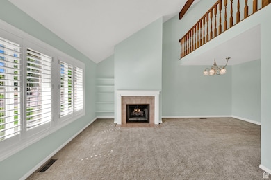 Unfurnished living room featuring carpet, a fireplace, high vaulted ceiling, built in shelves, and a chandelier