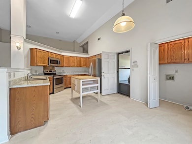 Kitchen with appliances with stainless steel finishes, high vaulted ceiling, brown cabinets, hanging light fixtures, and light stone counters
