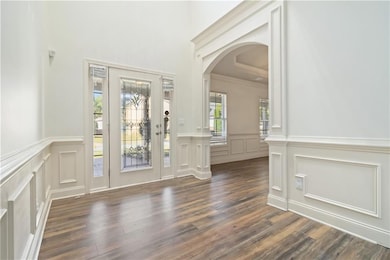Entryway featuring arched walkways, dark wood-style floors, a decorative wall, wainscoting, and crown molding