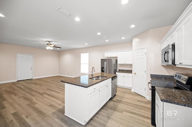 Kitchen featuring light wood-type flooring, white cabinetry, appliances with stainless steel finishes, sink, and a kitchen island with sink
