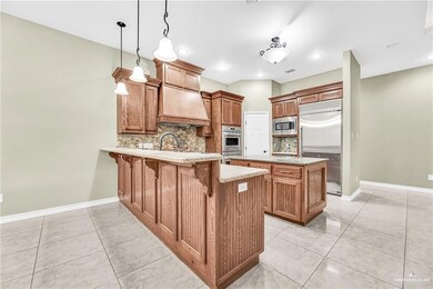 Kitchen featuring kitchen peninsula, tasteful backsplash, built in appliances, pendant lighting, and custom range hood