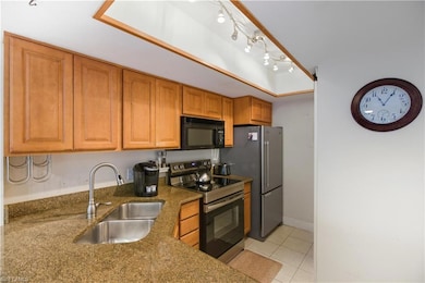 Kitchen with stainless steel range with electric stovetop, black microwave, light tile patterned flooring, brown cabinets, and dark stone countertops