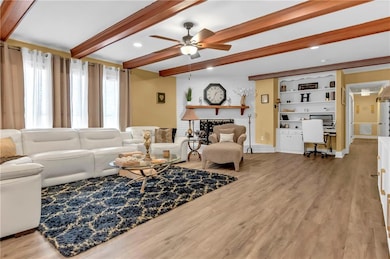 Living room featuring beamed ceiling, a ceiling fa